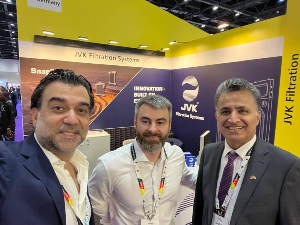 Three visitors and employees pose together in front of the JVK Filtration Systems stand. The stand showcases filtration technology "Made in Germany" and serves as a meeting point for technical discussions.