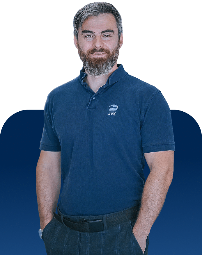 Freigestelltes Porträt eines Mitarbeiters von JVK Filtration Systems in einem dunkelblauen Poloshirt mit Logo. Die Person steht vor neutralem Hintergrund und wirkt professionell und selbstbewusst.